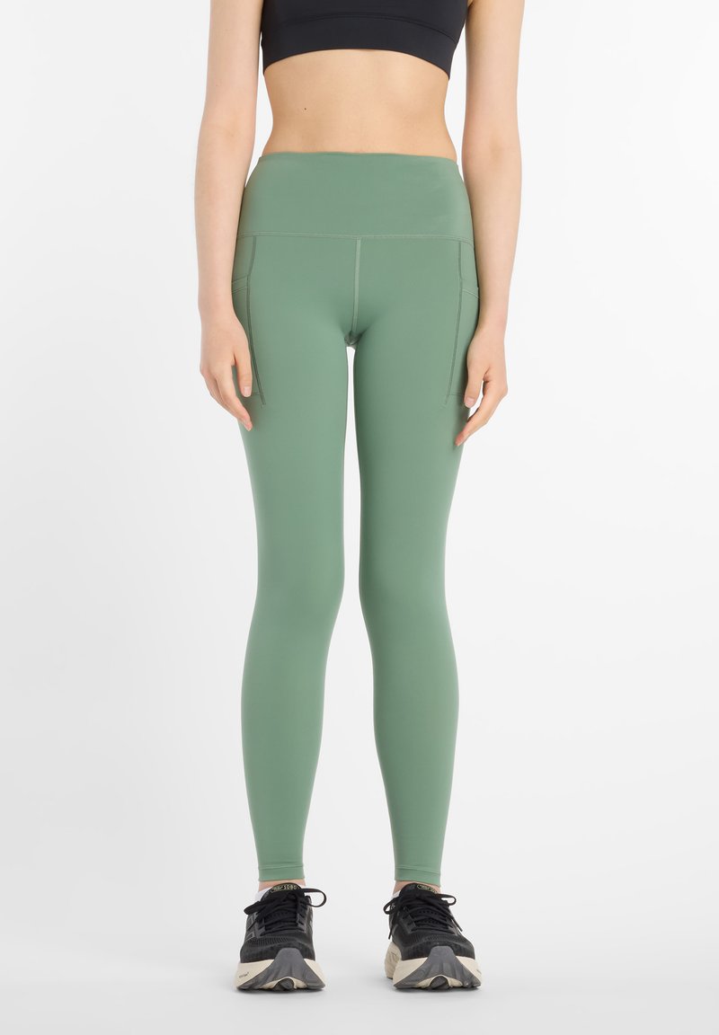 Leggings de talle alto y ajuste ceñido en un tono verde apagado, fabricados con material elástico, con bolsillos laterales y textura suave.