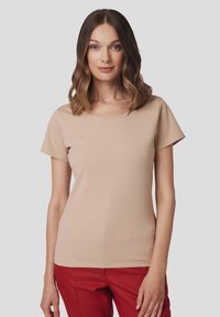 Beżowa koszulka z krótkim rękawem, okrągłym dekoltem, miękką teksturą, dopasowanym krojem i gładkim wykończeniem, w połączeniu z czerwonymi spodniami.