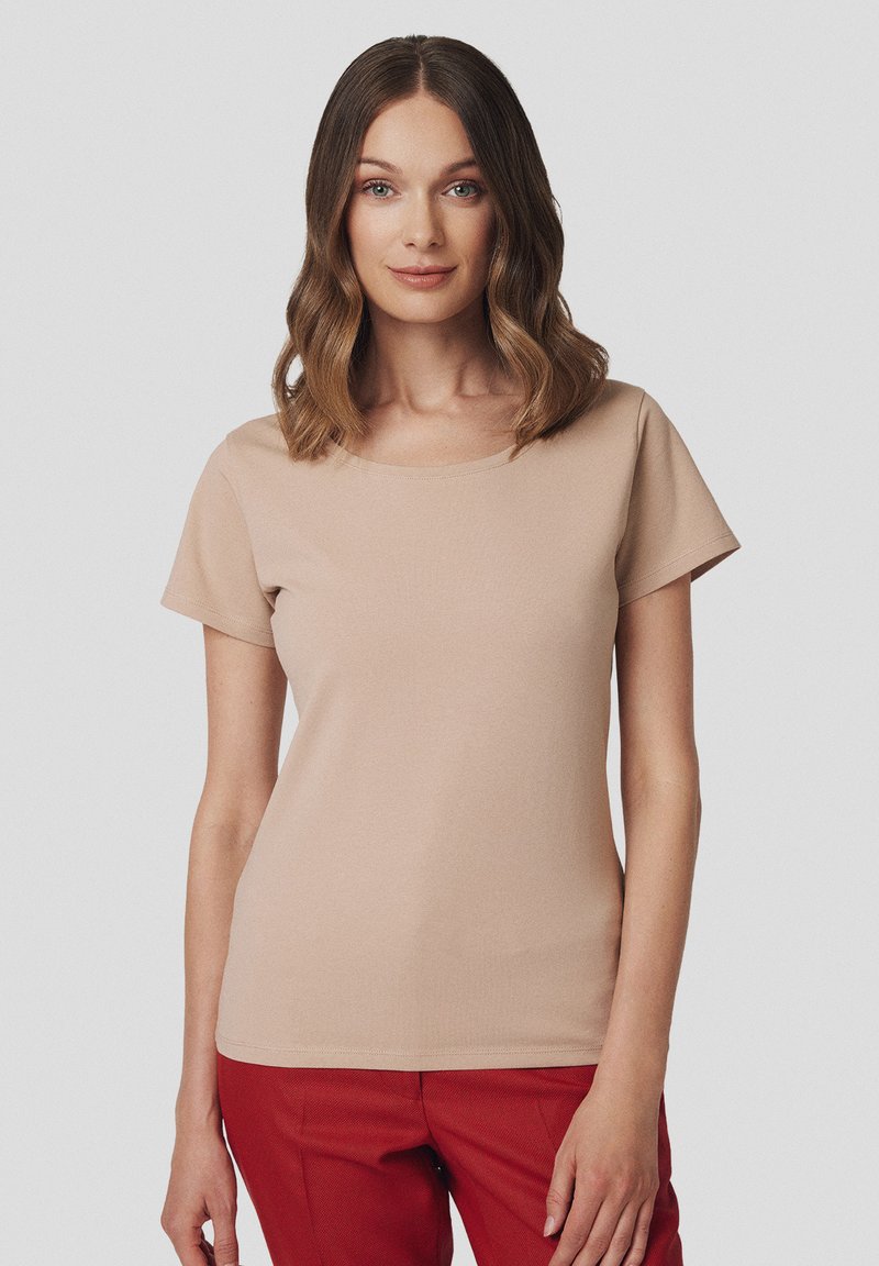 Beżowa koszulka z krótkim rękawem, okrągłym dekoltem, miękką teksturą, dopasowanym krojem i gładkim wykończeniem, w połączeniu z czerwonymi spodniami.