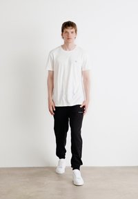 Λευκό μπλουζάκι με λαιμόκοψη, μαύρο παντελόνι φόρμας και άσπρα αθλητικά παπούτσια. Απλός σχεδιασμός, λεία υφή, με ένα μικρό λογότυπο στην μπλούζα.