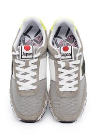Sneaker grigio e bianco con materiali in camoscio e rete, lacci bianchi piatti, suola stampata e un'emblema rosso del Giappone sulla linguetta.