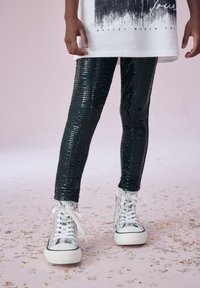 Leggings neri con paillettes dal design aderente, abbinati a sneakers alte argento con lacci bianchi e suole in gomma.
