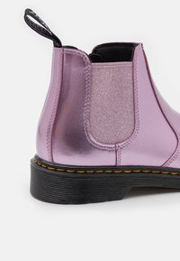 Lila metallisk Chelsea-stövel med glansig finish, elastiska sidor och en svart texturerad sula. Har en svart dragflik på hälen.
