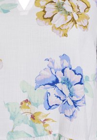Biely textil s veľkými, viacfarebnými kvetinovými vzormi v modrej, žltej a zelenej farbe. Štruktúra je mierne rebrovaná, čo poskytuje kontrast.