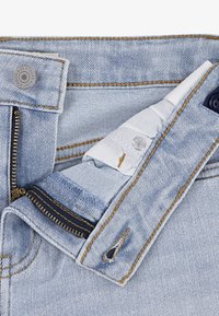 Hellblaue Jeans aus Denim mit sichtbarem Reißverschluss, Knopfverschluss und kontrastierenden Nähten. Der Stoff zeigt eine leichte Textur und hat einen normalen Bund.