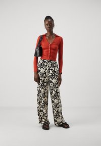 Rød langermet knappebluse, svarte bukser med blomsterprint og vid ben, svart skulderveske, flate sandaler. Glatt tekstur gjennom hele.