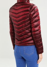 Rød quiltet pufferjakke har en høj krave, chevronmønster og en blank tekstur. At parre med blå jeans fuldender det afslappede look.