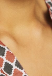 Tissu à motifs rouges et noirs présentant des formes géométriques, avec une texture lisse, mettant l'accent sur la zone du décolleté.
