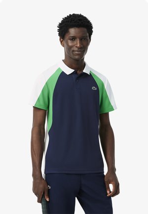 Polo shirt a maniche corte navy e verde con accenti bianchi e colletto; presenta un logo sul petto sinistro e una texture traspirante.