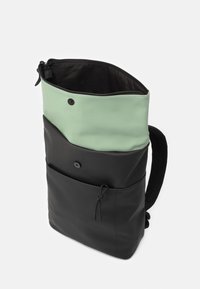 Ryggsäck med en mintgrön övre del och svart nedre del. Har en dragkedja, knappar, snörning och ett tygband.
