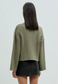Olivgrüner gerippter Pullover mit weiten Ärmeln, cropped Design und strukturiertem Stoff, kombiniert mit einem schwarzen Minirock.