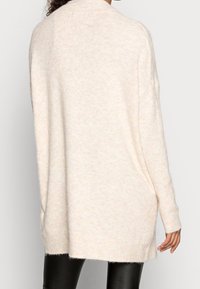 Vaaleanpunainen ylipitkä neulepusero, valmistettu pehmeästä neuloskankaasta, jossa on pyöreä pääntie ja tiputetut hartiat rentoa istuvuutta varten.