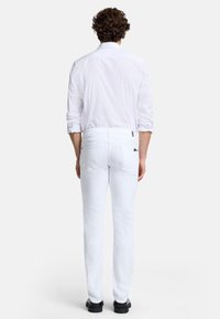 Jean blanc ajusté, fabriqué en denim. Comprend des poches standard et une texture lisse. Associé à une chemise blanche et des chaussures noires.