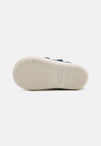 Navy shoe sole with a textured white rubber outsole, featuring horizontal and vertical grooves for grip and the logo embossed in the center.