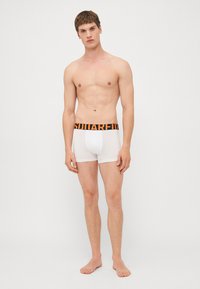 White cotton boxer briefs with a black elastic waistband featuring orange lettering. The design is fitted and smooth, with a mid-thigh length.