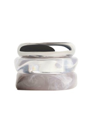 Tre stablede ringe med glatte overflader, herunder en sølvmetallisk ring, en klar gennemsigtig ring og en marmoreret lys grå ring.