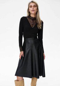 Czarna bluzka z długimi rękawami z koronkowymi detalami przy dekolcie i mankietach, zestawiona z czarną skórzaną spódnicą w kształcie dzwonu. Teksturowany materiał; dopasowana talia.