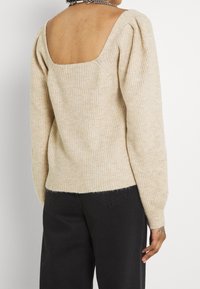 Maglione beige a costine con scollatura quadrata e maniche a sbuffo, caratterizzato da un tessuto testurizzato e da una silhouette aderente. Abbinato a pantaloni scuri.
