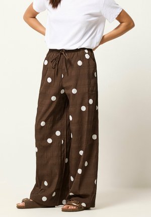Brązowe spodnie z szerokimi nogawkami i dużymi białymi groszkami, zestawione z białym topem z krótkim rękawem i brązowymi sandałami na klamrę.
