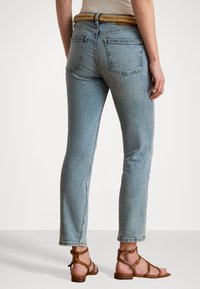 Ljusblå denimjeans med rak skärning, med hög midja, två bakfickor och ett vävt repbälte, i kombination med bruna sandaler med remmar.