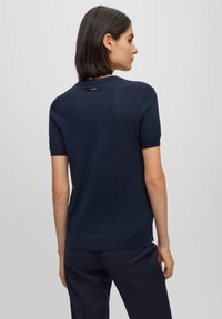 Navyblaues, gestricktes T-Shirt mit kurzen Ärmeln und rundem Ausschnitt, mit einem Logo-Detail auf der Rückseite und gerippten Kanten. Glatte Textur.