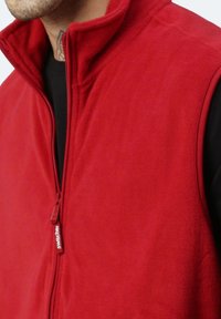 Rote Fleece-Weste mit hohem Kragen, verfügt über einen Reißverschluss vorne und ein kleines Logotag am Reißverschluss. Weiche Textur und lässige Passform.