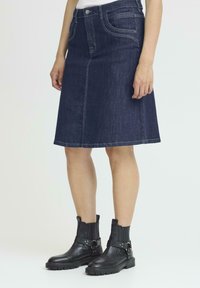 Jeans A-linje kjol i mörkblå färg, knä-längd med fickor och sydda detaljer. Kombinerad med svarta ankelstövlar med spännen.