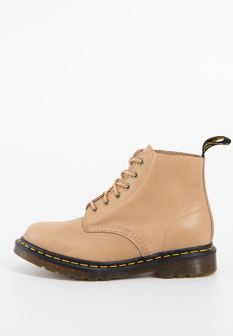 Botín de cuero beige hasta el tobillo con diseño de cordones, puntera redonda, costuras amarillas y suela de goma negra. Cuenta con una lengüeta en el talón.