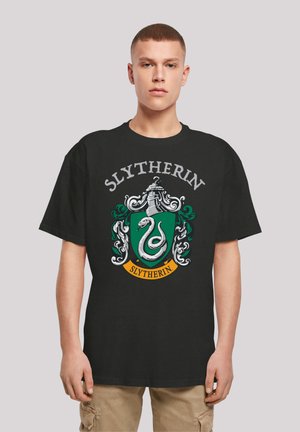 Black t-shirt featuring Slytherin house crest in green, silver, and white, with a snake and decorative elements. Short sleeves, round neck.