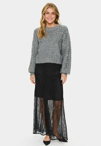 Maglione grigio a maglia con scollatura rotonda e dettagli in perle, abbinato a una gonna maxi nera in pizzo con uno strato trasparente.