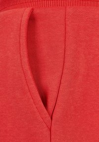 Tejido de algodón rojo con una superficie ligeramente texturizada, que presenta una abertura de bolsillo profunda y una cinturilla acanalada.