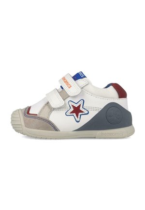 Zapatilla infantil blanca y gris con diseño de estrella roja y azul, dos tiras de Velcro y zonas reforzadas en el talón y la puntera.