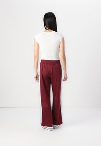 Weißes, figurnahes Oberteil und bordeauxfarbene, weit geschnittene Hose mit weißen Seitenstreifen. Elastischer Bund und Taschen im Rücken der Hose.
