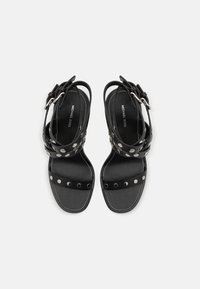Μαύρα δερμάτινα σανδάλια με πολλαπλές ρυθμιζόμενες λουρίδες στον αστράγαλο, με ασημένιες λεπτομέρειες και επίπεδη σόλα. Ο λογότυπος της μάρκας είναι ορατός στο εσωτερικό.