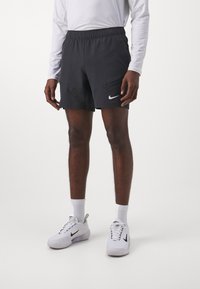 Pantalones cortos deportivos negros con cintura elástica, dos bolsillos laterales y un logo de Nike en blanco. Llevados con zapatillas blancas y calcetines de caña.