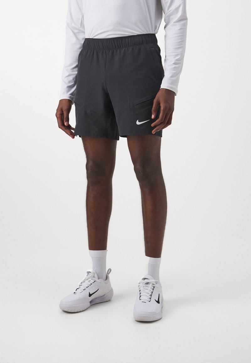 Pantalones cortos deportivos negros con cintura elástica, dos bolsillos laterales y un logo de Nike en blanco. Llevados con zapatillas blancas y calcetines de caña.