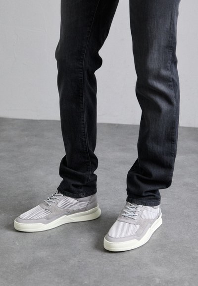 Light gray sneakers with mesh upper, suede accents, and white rubber sole, paired with dark denim jeans. Features a lace-up design.