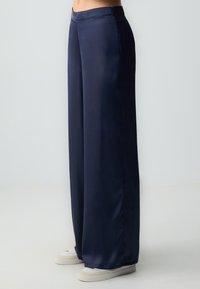 Pantalons large en navy en tissu lisse avec une taille haute et des poches latérales, associés à des baskets blanches.