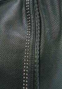 Zwarte leren tas met geperforeerde textuur, een gevlochten accent langs de naad en een rij zilveren studs voor details.