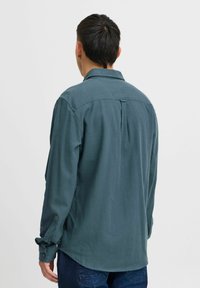 Langermet, teal skjorte med klassisk krage, teksturert stoff, bakfold detaljer og knappede mansjetter. Brukt sammen med mørke jeans.