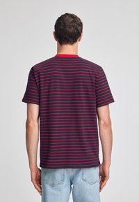 Mörkblå kortärmad t-shirt med röda horisontella ränder och röd krage. Tillverkad av bomull, avslappnad passform, synliga sömmar vid axlarna.