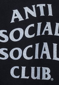 Czarna koszulka z wyraźnym, błyszczącym srebrnym napisem "ANTI SOCIAL SOCIAL CLUB" w zakrzywionym układzie.