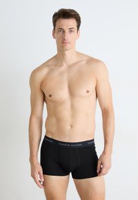 Fekete pamut boxer alsónadrág logós derékrésszel, testhezálló fazonnal és sima textúrával. A modellen mezítelen felsőtesttel van látható.