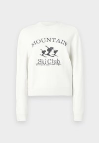 Balts īss sporta džemperis ar apaļu kakla izgriezumu, garām piedurknēm un grafisku attēlu ar slēpotājiem un uzrakstu "MOUNTAIN Ski Club".