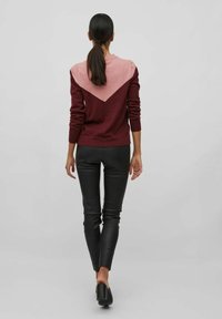 Burgundy och rosa färgblockerad tröja med en V-formad design på baksidan, tillverkad av stickat material, i kombination med släta svarta läderbyxor.