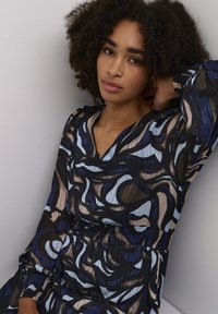 Langarmkleid mit einer Mischung aus blauen, braunen und schwarzen abstrakten Mustern. V-Ausschnitt mit strukturiertem Stoff und gerafftem Taillendetail.