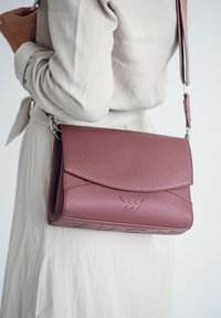 Rosa Lederhandtasche mit umgeschlagenem Deckel, silbernem Zubehör und geprägtem Logo. Verstellbarer Tragegurt und glatte Textur mit minimaler Naht.