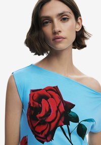 Kék, vállnélküli felső sima anyagból, nagy piros rózsa grafikával és levelekkel, melyek éles kontrasztot és részletgazdagságot alkotnak.