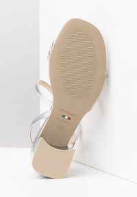 Sandale argentée à lanières avec une semelle lisse, un talon profilé et un dessous texturé pour une bonne adhérence. Elle présente une étiquette de marque et une étiquette "Italie" de taille 37.