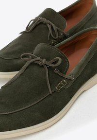 Scarpe in suede verde oliva con una texture liscia, caratterizzate da un design con lacci, suola in gomma bianca e dettagli di cucitura decorativa.